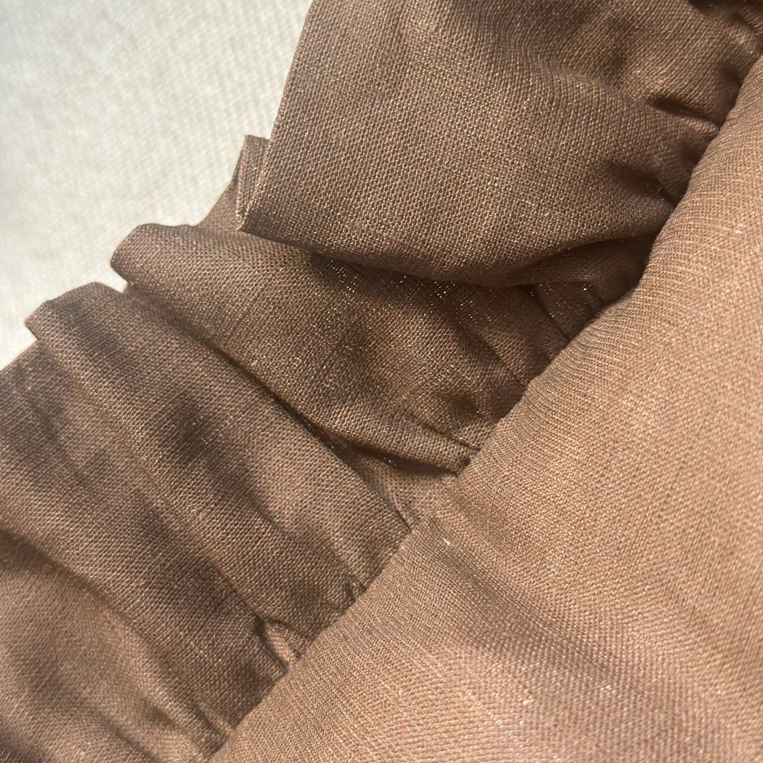 Close-up of a brown fabric garment with gathered ruffle detailing and a textured woven material.