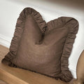 A brown ruffled decorative throw pillow resting on a wooden bench against a white wall.