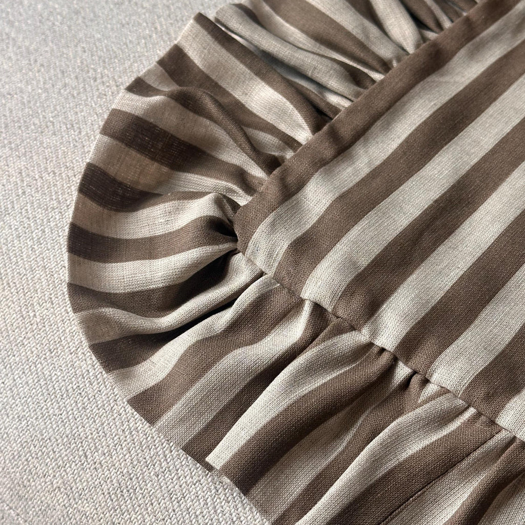 Close-up of a striped fabric product with ruffled edges, featuring alternating brown and beige horizontal stripes on a light textured background.