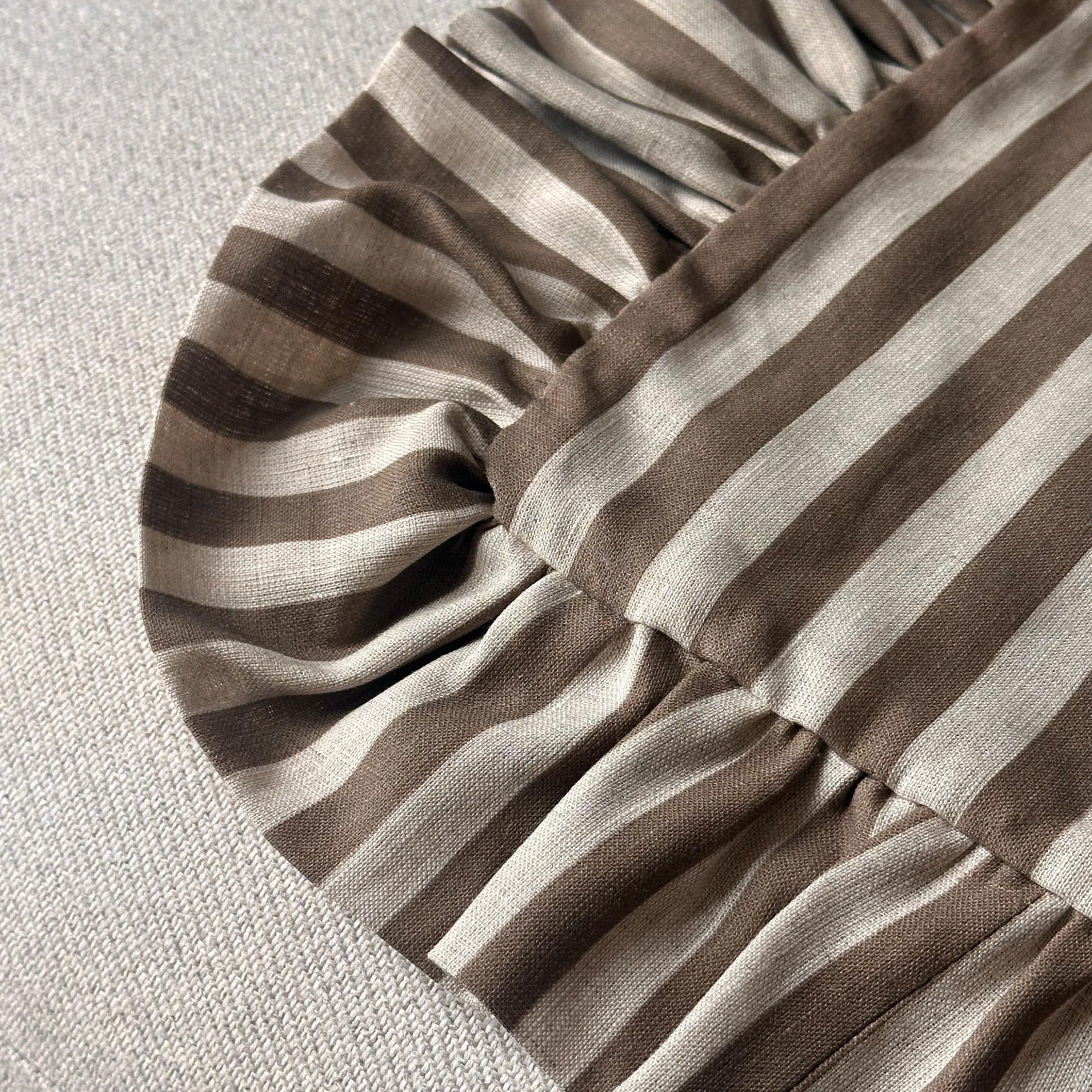 Close-up of a striped fabric product with ruffled edges, featuring alternating brown and beige horizontal stripes on a light textured background.